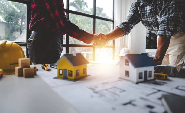 2 person handshake with mini house display and blueprint of house on table -general construction