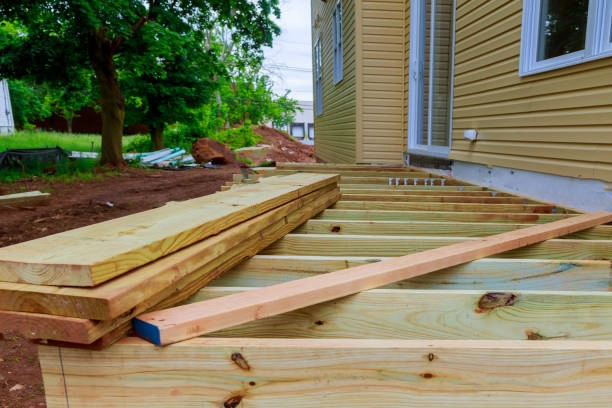 Wooden deck construction in progress with stacked boards, near house. -constructed decks