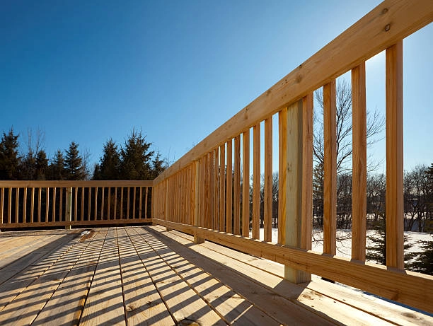 Wooden deck with vertical railing, casting shadows under clear skies. -deck railing construction