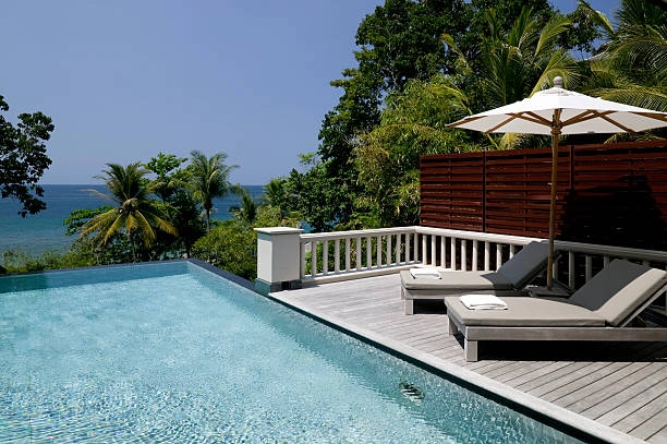 Infinity pool with ocean view, wooden deck, and lounge chairs. -pool deck construction plans