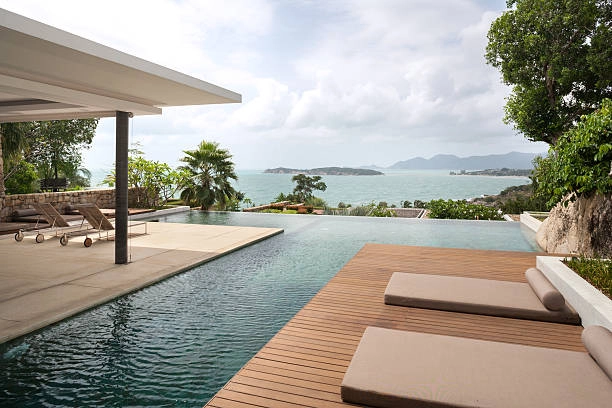 Infinity pool with wooden deck, lounge chairs, and ocean view. -pool deck construction plans