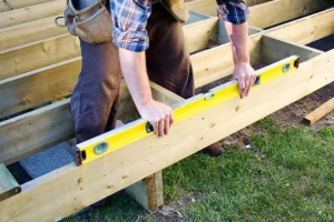 Person leveling wooden beams while constructing a deck foundation. -deck construction guide