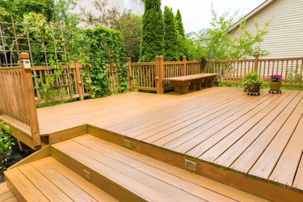 Multi-level wooden deck with built-in bench, surrounded by greenery. -deck construction guide