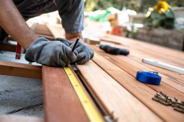 Worker measuring and marking wood for deck construction with tools nearby. -decking contractor