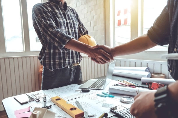 Handshake between contractors finalizing a construction agreement over blueprints. -general construction services